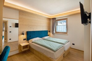 Ein Schlafzimmer mit zwei Betten, einem Fernseher, einem Fenster mit Vorhängen und einer Holzbalkendecke.
