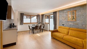 A modern living room with a sofa, dining table, chairs, and a TV. - Chalet 'Arnica' with Mountain View, Balcony and Wi-Fi (Livigno)