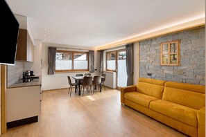 A modern living room with a sofa, dining table, chairs, and a TV. - Chalet 'Arnica' with Mountain View, Balcony and Wi-Fi (Livigno)
