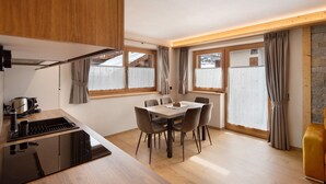 A modern kitchen with a dining area, wooden cabinets, a stove, and a table with chairs. - Chalet 'Arnica' with Mountain View, Balcony and Wi-Fi (Livigno)