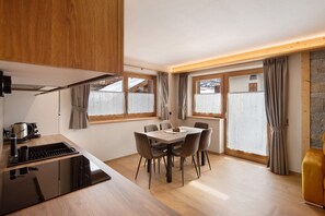 A modern kitchen with a dining area, wooden cabinets, a stove, and a table with chairs. - Chalet 'Arnica' with Mountain View, Balcony and Wi-Fi (Livigno)