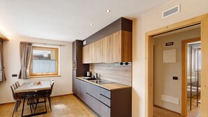 A modern kitchen with a dining table, wooden cabinets, and a window. - Chalet 'Genziana' with Mountain View, Balcony and Wi-Fi (Livigno)