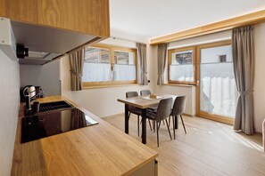 A compact kitchen with a dining area, wooden cabinets, and large windows with curtains. - Chalet 'Timo' with Mountain View, Private Terrace and Wi-Fi (Livigno)