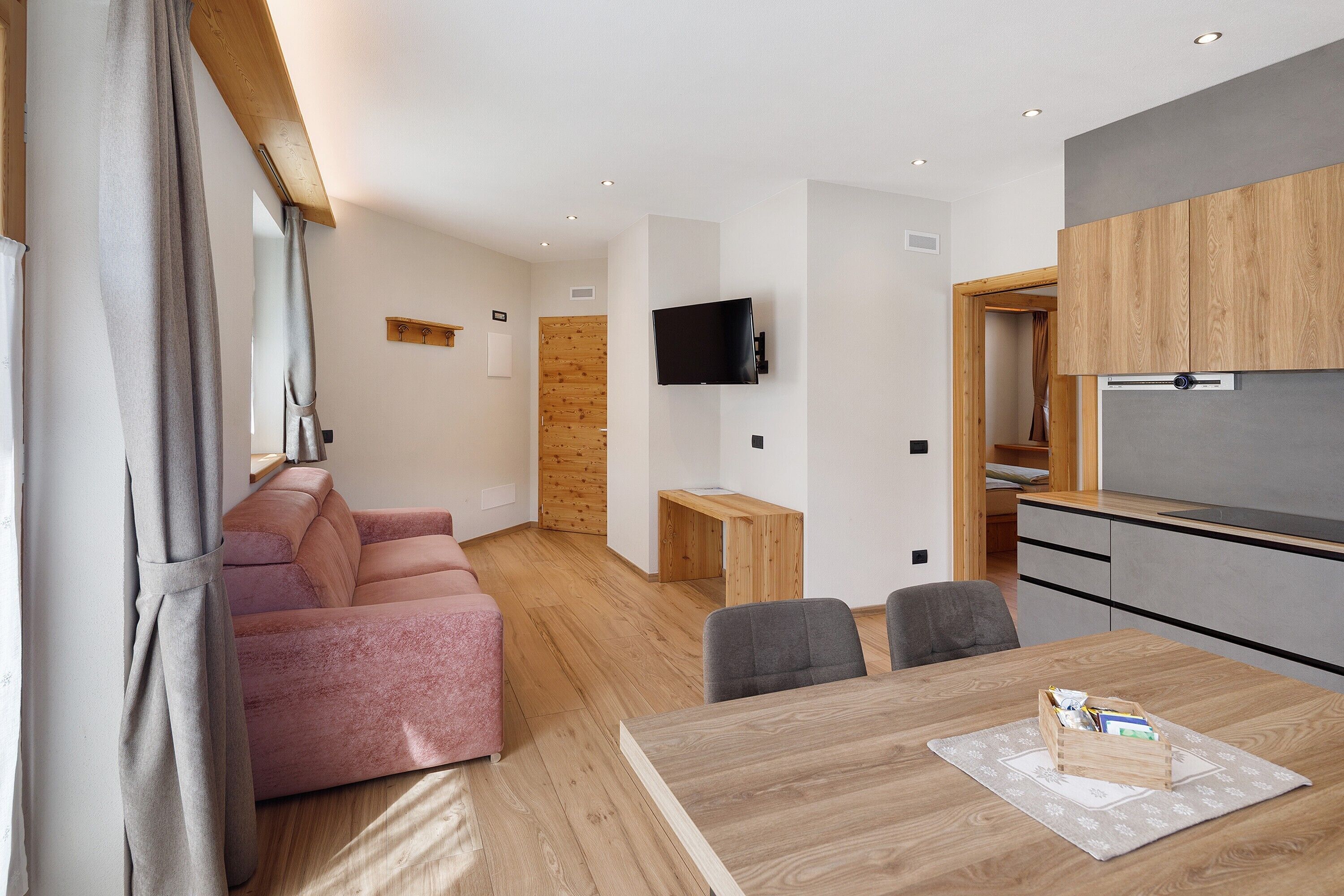 Una sala de estar moderna con un sofá, una mesa de comedor con sillas, una zona de cocina y un televisor montado en la pared.