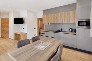 A modern kitchen with wooden cabinets, a built-in microwave, and a dining area with a wooden table and chairs. - Chalet 'Timo' with Mountain View, Private Terrace and Wi-Fi (Livigno)