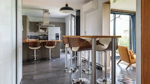 A modern kitchen with bar stools, a dining table, and a view of the adjacent living area.