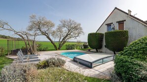 A house with a swimming pool, a garden, and a view of the countryside.