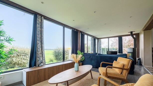 A modern living room with a sofa, a coffee table, and a view of the outdoors through large windows.