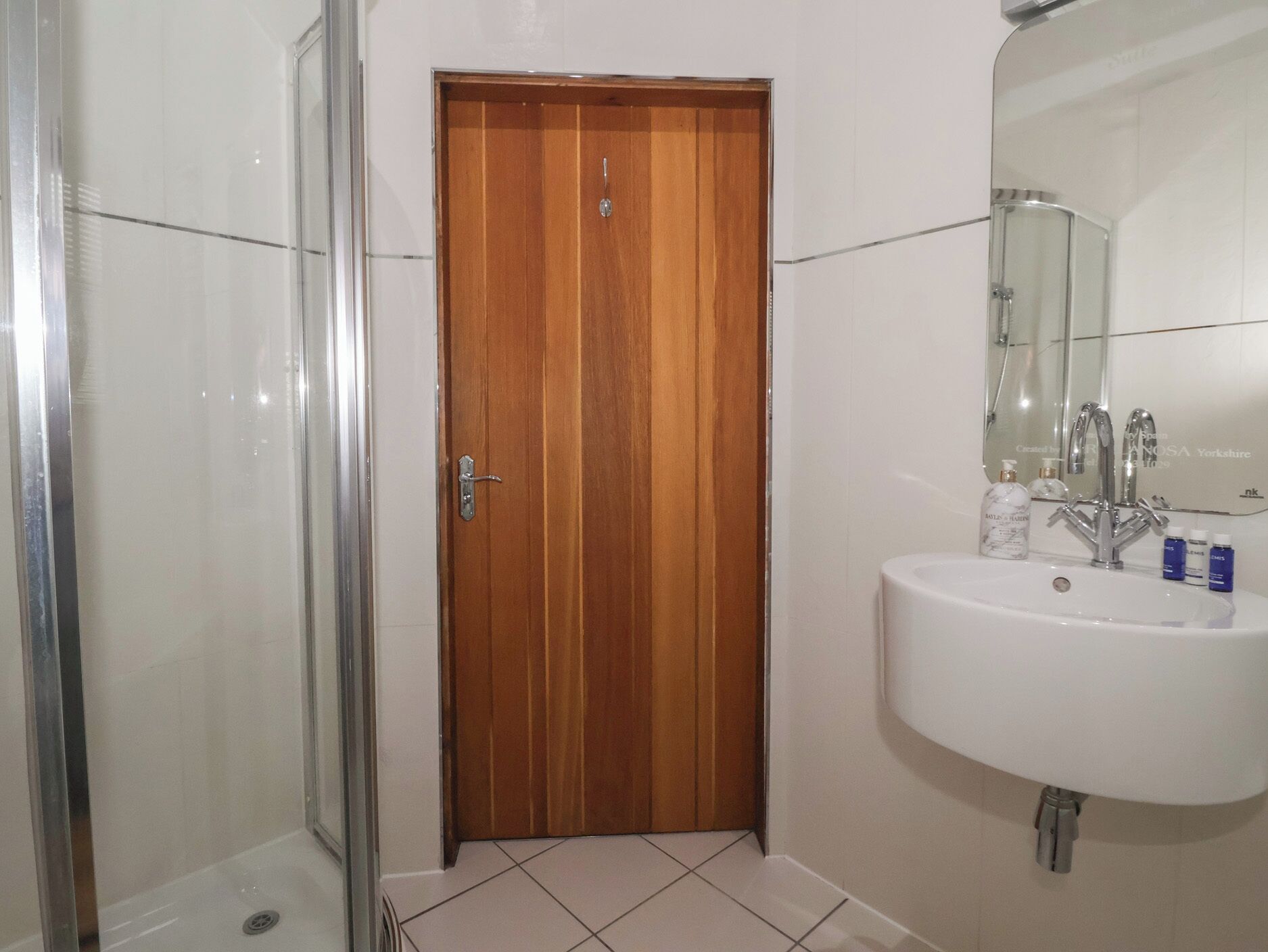A bathroom with a wooden door, a glass shower enclosure, and a white sink with a mirror.