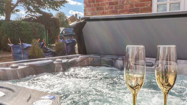 Een jacuzzi met twee champagneglazen, omringd door een bakstenen muur en een haag.