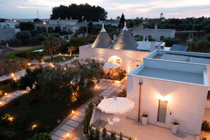 A modern building with a courtyard, featuring a dining area with outdoor seating and a large umbrella. - Apulian Charme Trulli & Cottage (Grazia) (Martina Franca TA)
