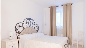 Ein Schlafzimmer mit einem Bett, einem Nachttisch, einem Sessel und einem Fenster mit Vorhängen.