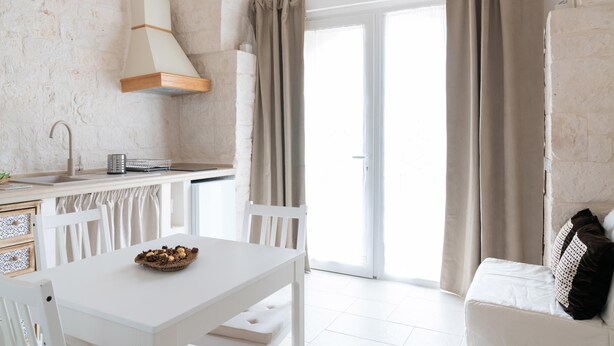 A modern kitchen with white cabinetry, a dining table with a basket of fruit, and a white chair. - Apulian Charm STELLA (Martina Franca TA)
