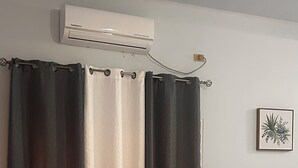 Un dormitorio con cama, cortinas, un equipo de aire acondicionado y un cuadro en la pared.