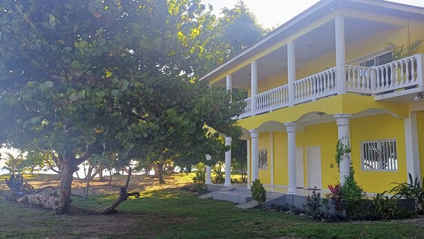 Un edificio amarillo con balcones y columnas blancos, rodeado de vegetación.