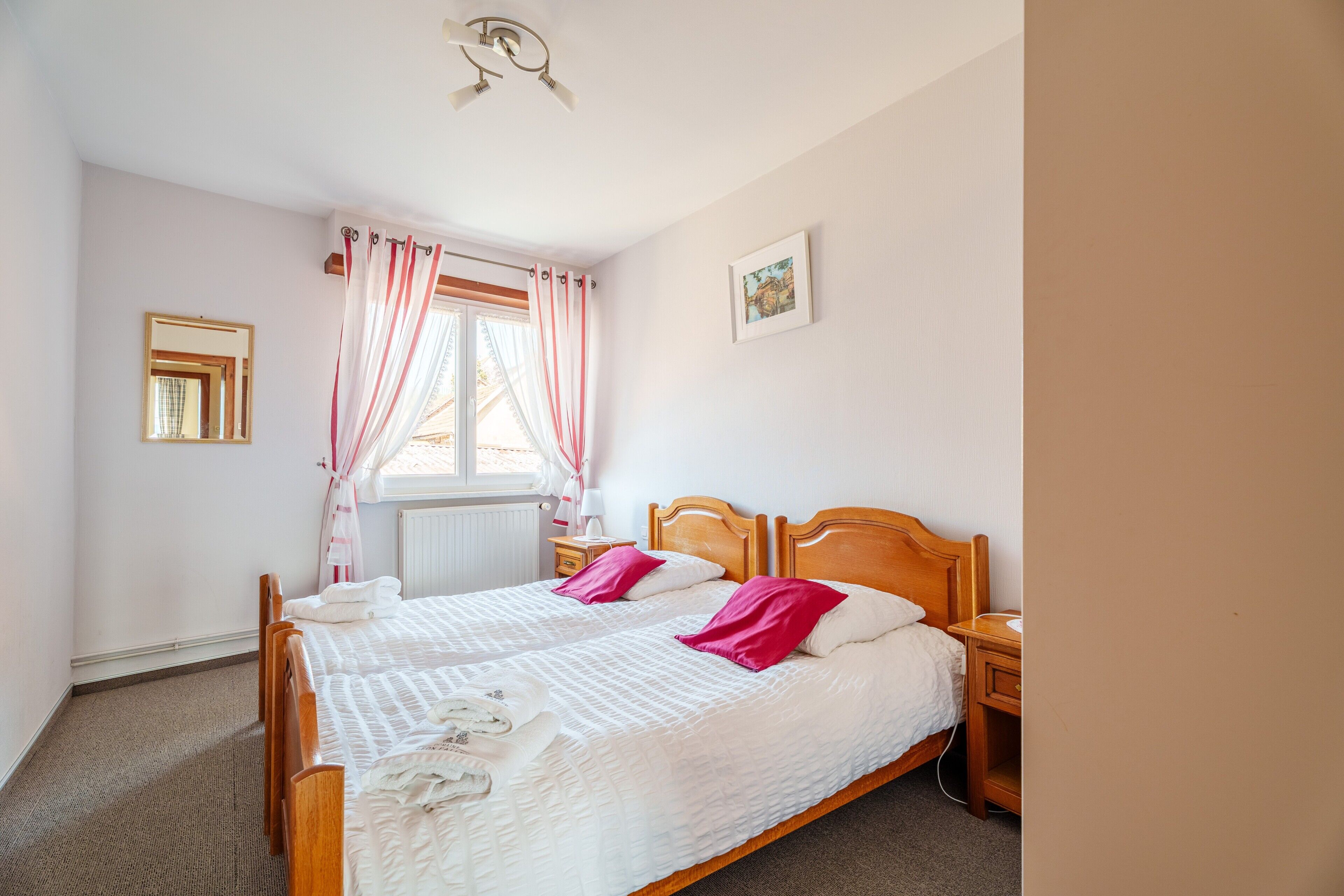 Een slaapkamer met een houten bed, een nachtkastje, een raam met gordijnen, een radiator en een lijst met een foto aan de muur.