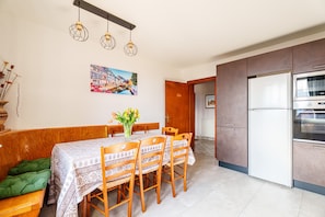 Un comedor con una mesa preparada para cuatro personas, un sofá verde y una cocina con refrigerador y horno.