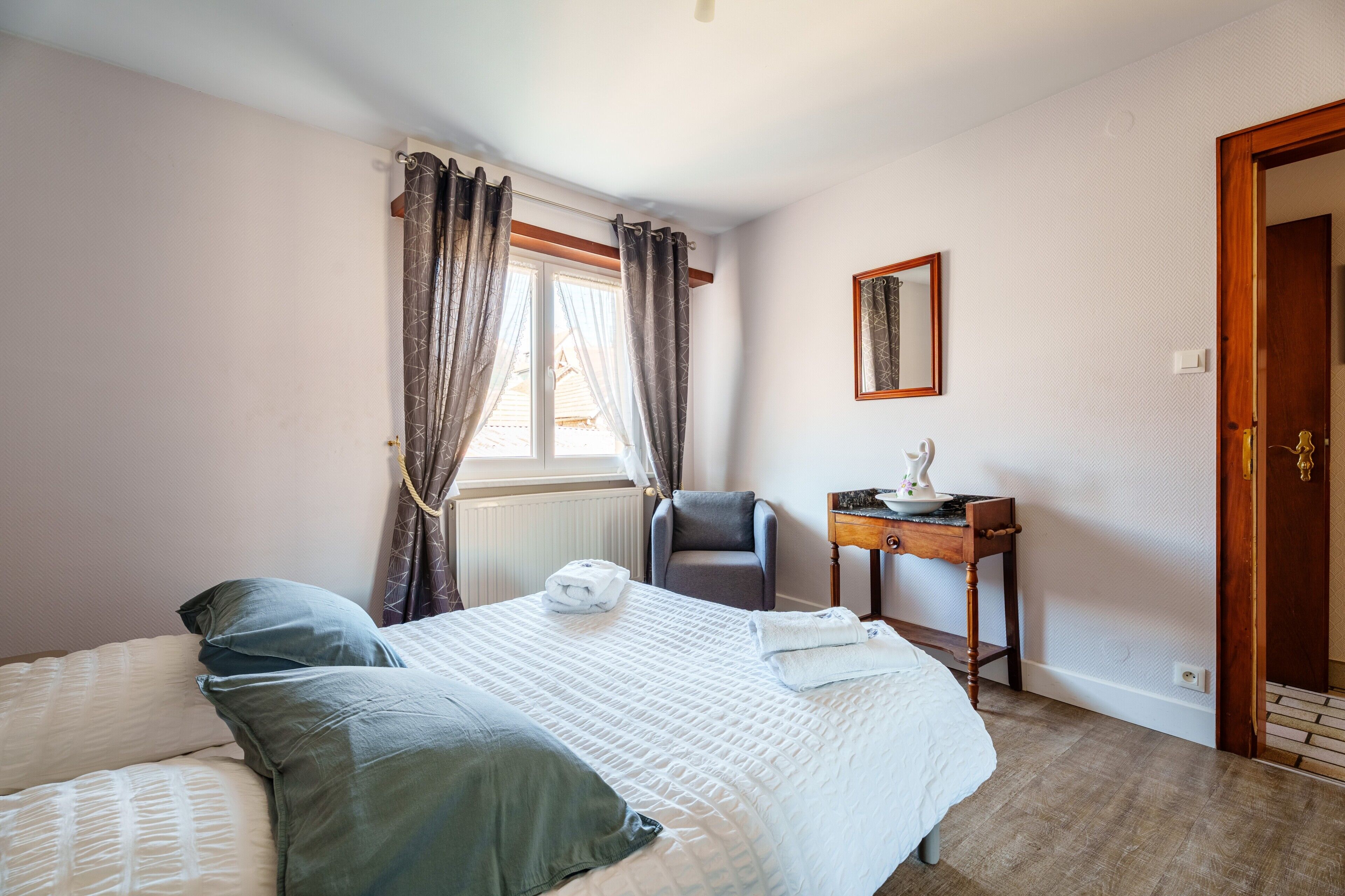 A bedroom with a bed, a chair, a table, a mirror, and a door.