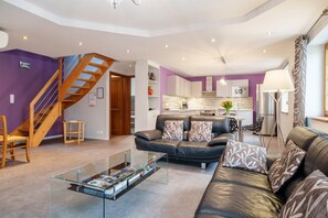 Un salon moderne avec un escalier, un canapé en cuir, une table basse en verre et une cuisine en arrière-plan.