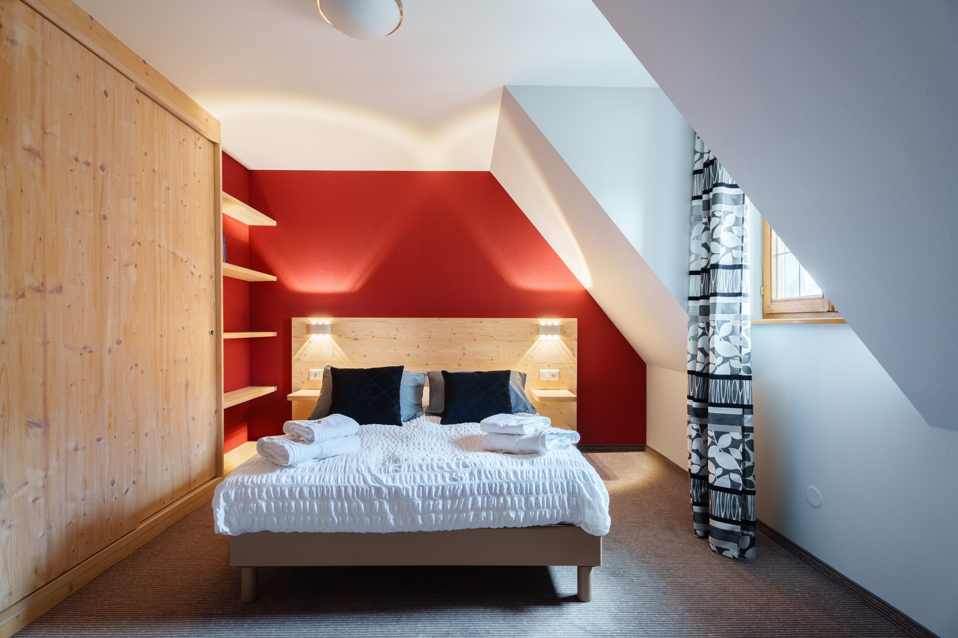 A bedroom with a bed, wooden wardrobe, red walls, and a sloped ceiling.