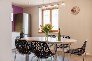 Une cuisine moderne avec un grand réfrigérateur, une table à manger avec des chaises, un vase de fleurs et une horloge au mur.