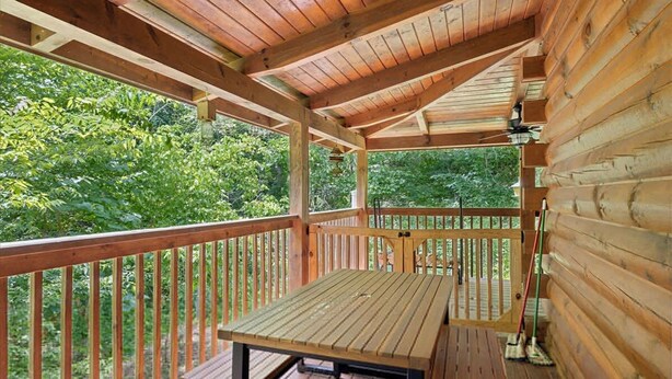 Une terrasse en bois, agrémentée d’une table et de chaises, entourée de murs en bois et d’une rambarde, et offrant une vue sur une zone boisée.