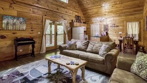 A cozy cabin interior with a wooden ceiling, a sofa, a coffee table, a refrigerator, and a dining area. - Stairway to Heaven by Beyond Expectations (Sevierville)