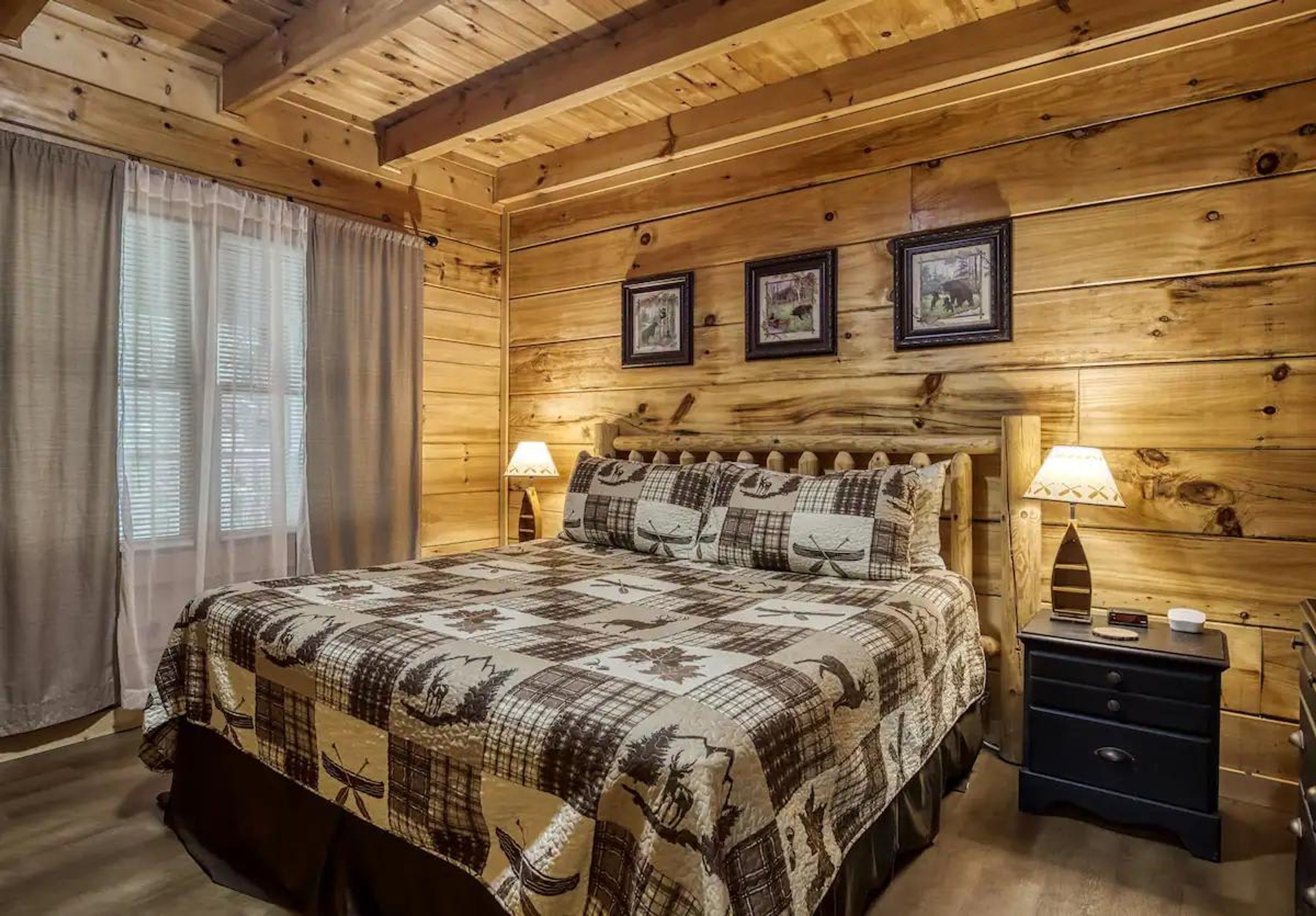 A wooden cabin bedroom with a bed, two bedside tables, and framed pictures on the wall.