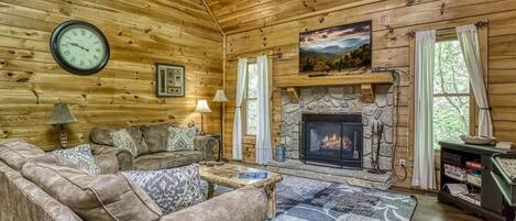 A log cabin interior with a stone fireplace, wooden walls, a sofa, and a clock.