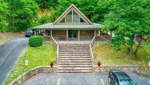 A cabin with a stone staircase leading to a wooden front door, surrounded by lush greenery. - Stairway to Heaven by Beyond Expectations (Sevierville)