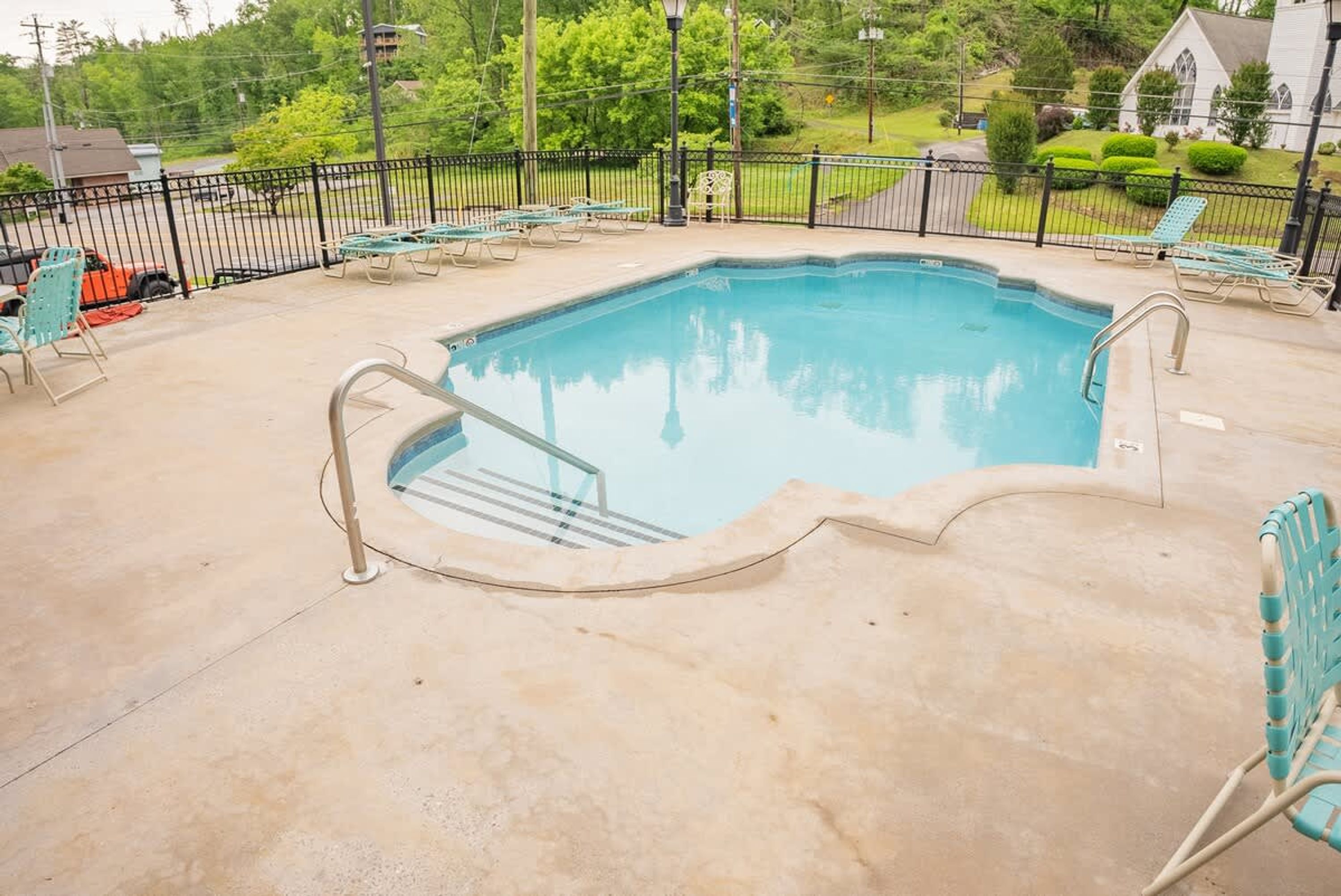 A rectangular swimming pool with a concrete deck, surrounded by a black metal fence, and equipped with a metal staircase leading into the pool.