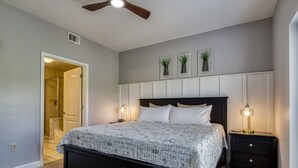 A bedroom with a bed, bedside tables, a ceiling fan, and a door leading to a bathroom. - Mountain View Condo by Beyond Expectations (Pigeon Forge)