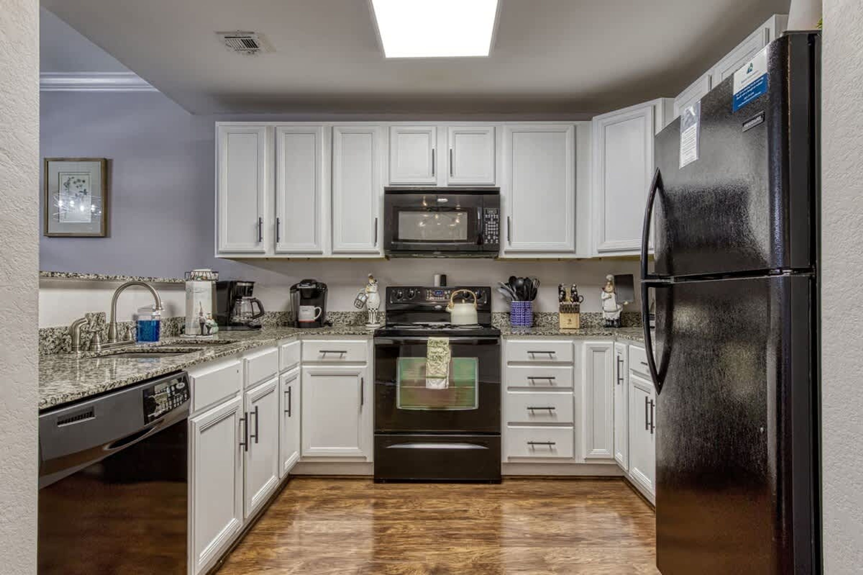 A kitchen with white cabinets, a black refrigerator, a microwave, and a stove.