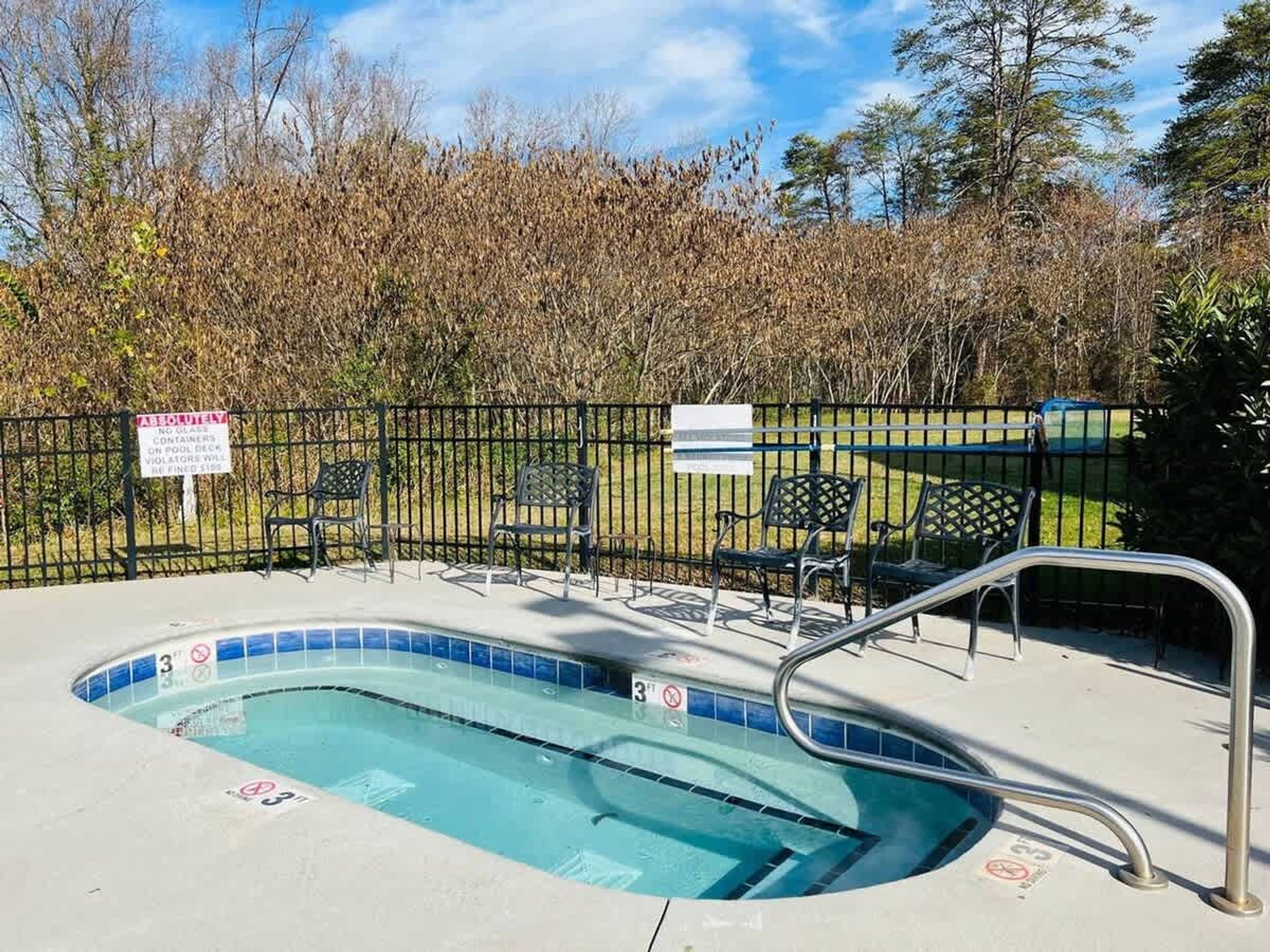 A swimming pool with a metal safety railing, surrounded by a fence and benches.