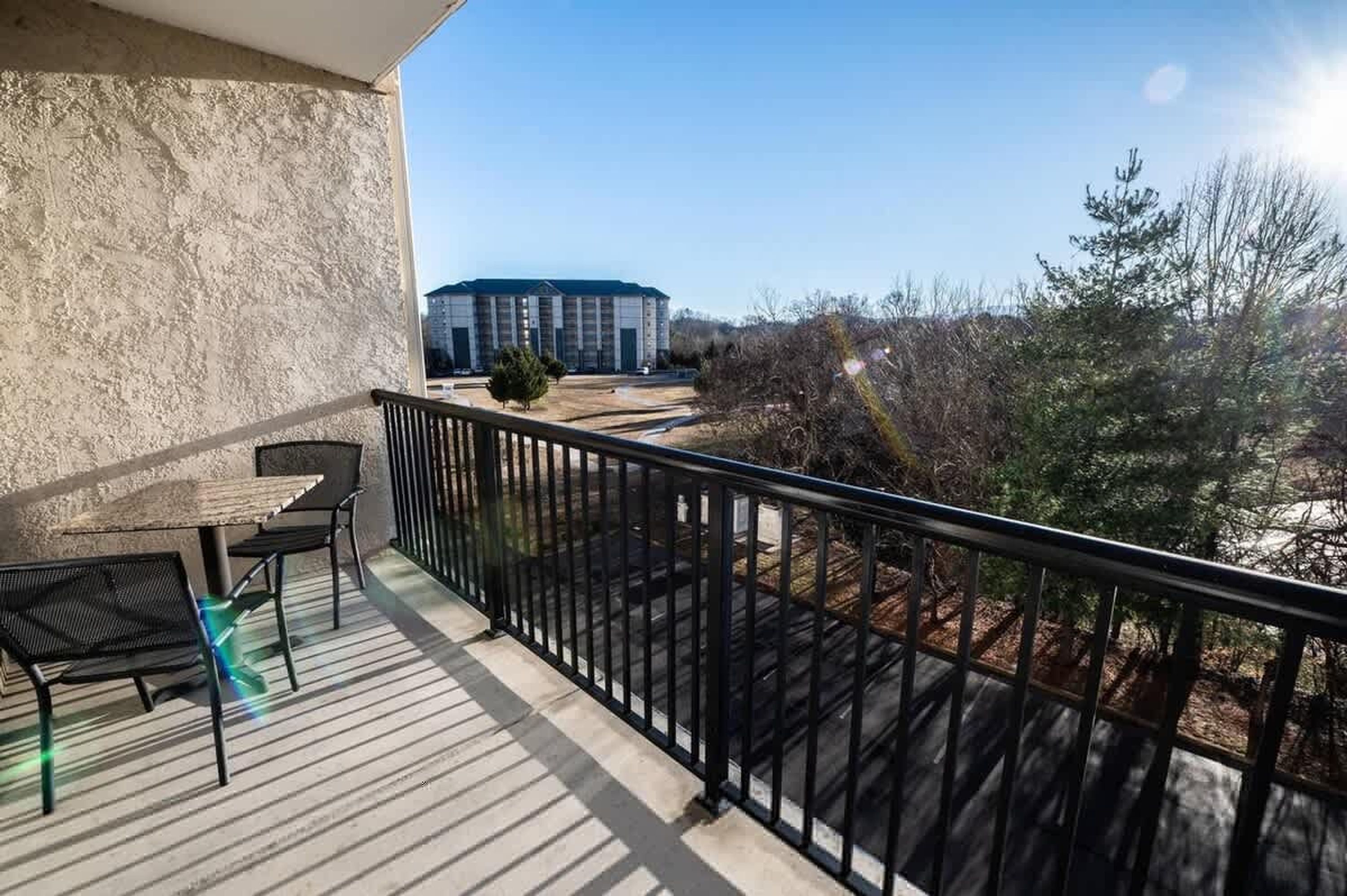 A balcony with a table and chairs, a view of a building, and surrounding vegetation.