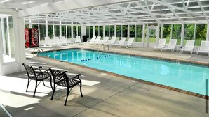 An indoor swimming pool with clear glass walls, white lounge chairs, and a Coca-Cola advertisement. - Mountain View Condo by Beyond Expectations (Pigeon Forge)