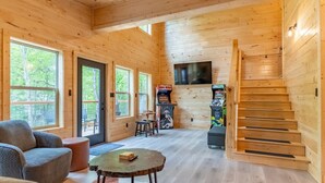 L’intérieur d’un chalet accueillant, avec des murs en bois, un canapé, une table basse, un téléviseur fixé au mur et un escalier.