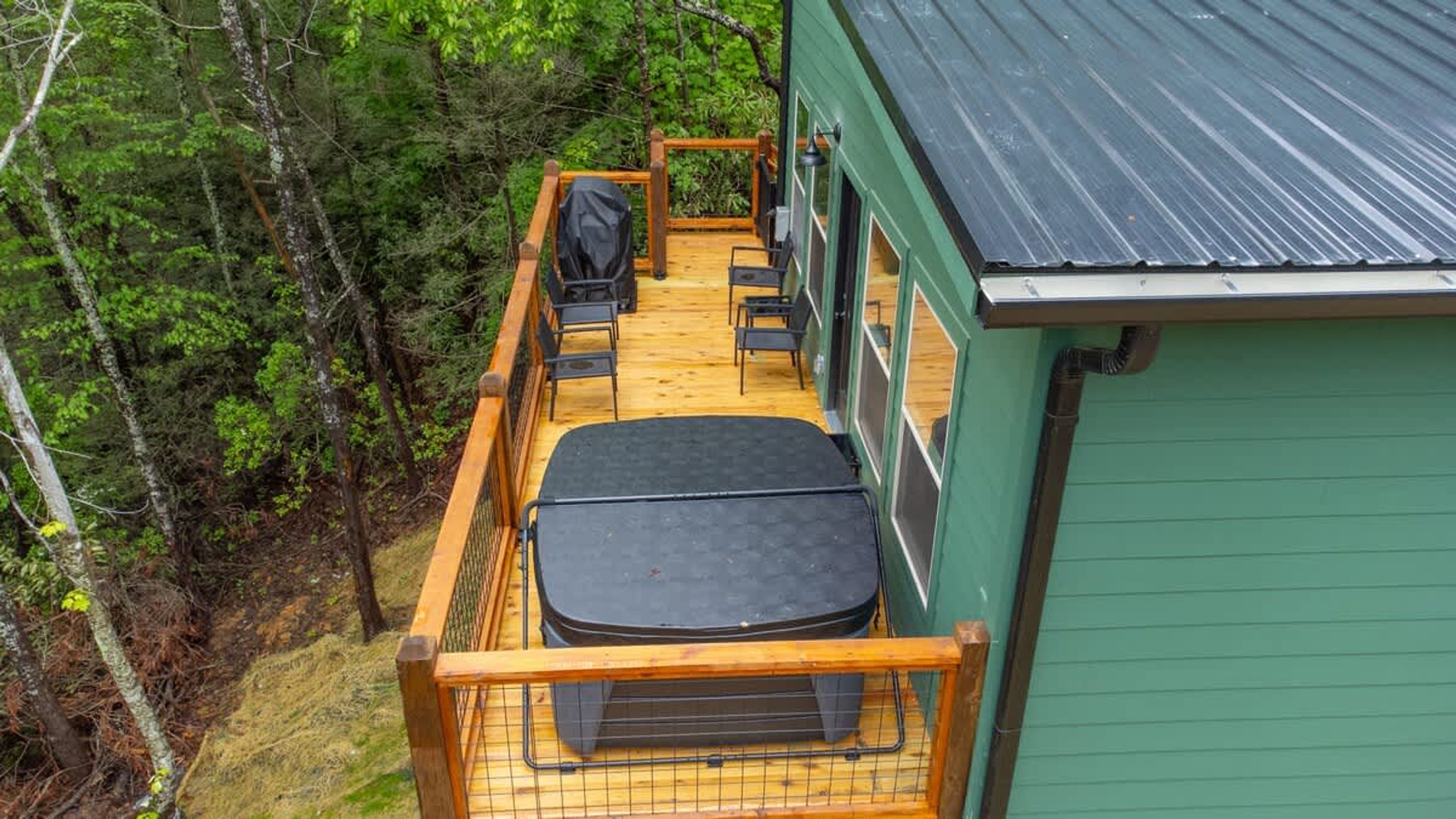 A wooden deck with a black outdoor seating area, surrounded by dense forest.