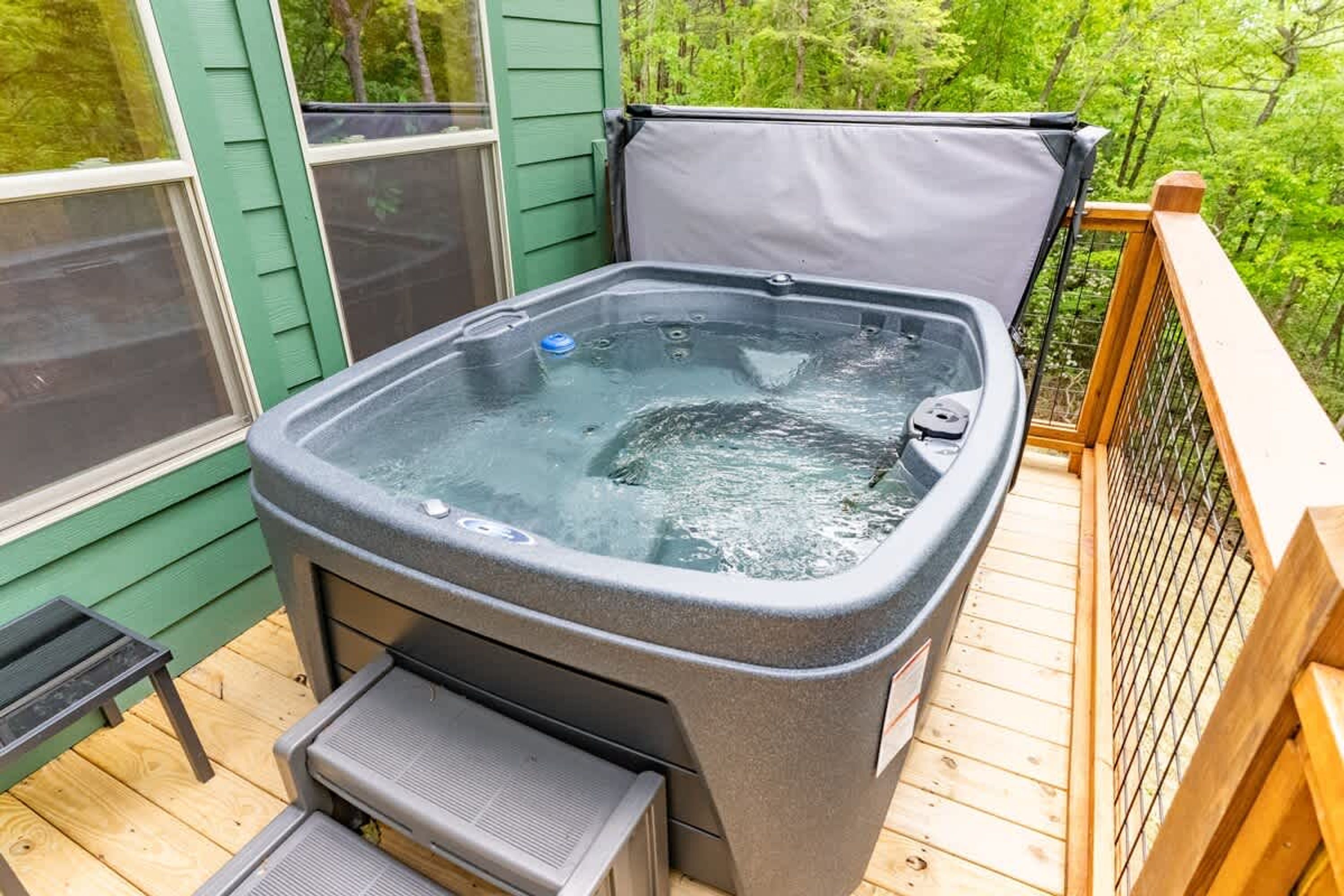 A hot tub on a wooden deck with a metal railing and a green wall in the background.
