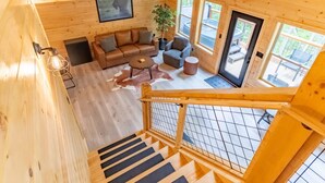 L’intérieur d’un chalet en bois comprend un canapé, des fauteuils, une table basse et un escalier menant à une terrasse.