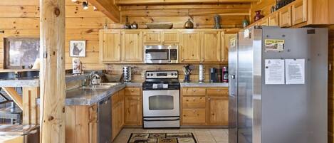 A wooden cabin-style kitchen with a stainless steel refrigerator, a microwave, an oven, and wooden cabinets.