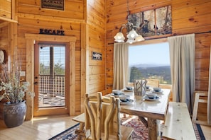 Ein Holzhäuschen-Interieur mit einem Esstisch, gedeckt für vier Personen, einem großen Fenster mit Aussicht und einer Tür mit der Aufschrift 'ESCAPE'.