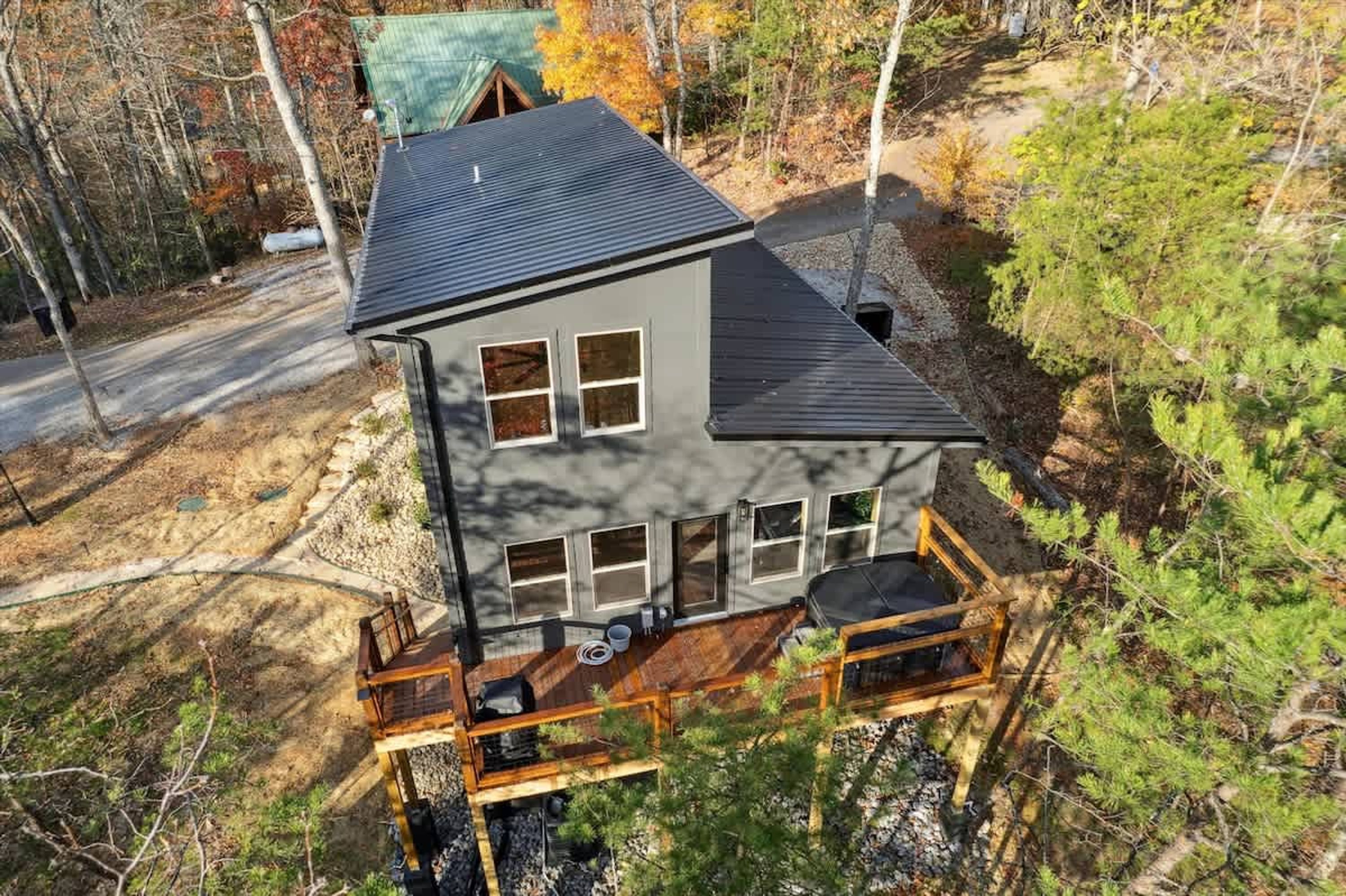 A two-story house with a deck, surrounded by trees and a gravel path.