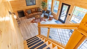 A wooden interior with a sofa, armchairs, a coffee table, and a staircase. - Green Black Bear Cabins by Beyond Expectations (Sevierville)