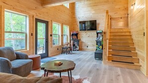 A cozy cabin interior with wooden walls, a sofa, a coffee table, a TV, and a staircase. - Green Black Bear Cabins by Beyond Expectations (Sevierville)