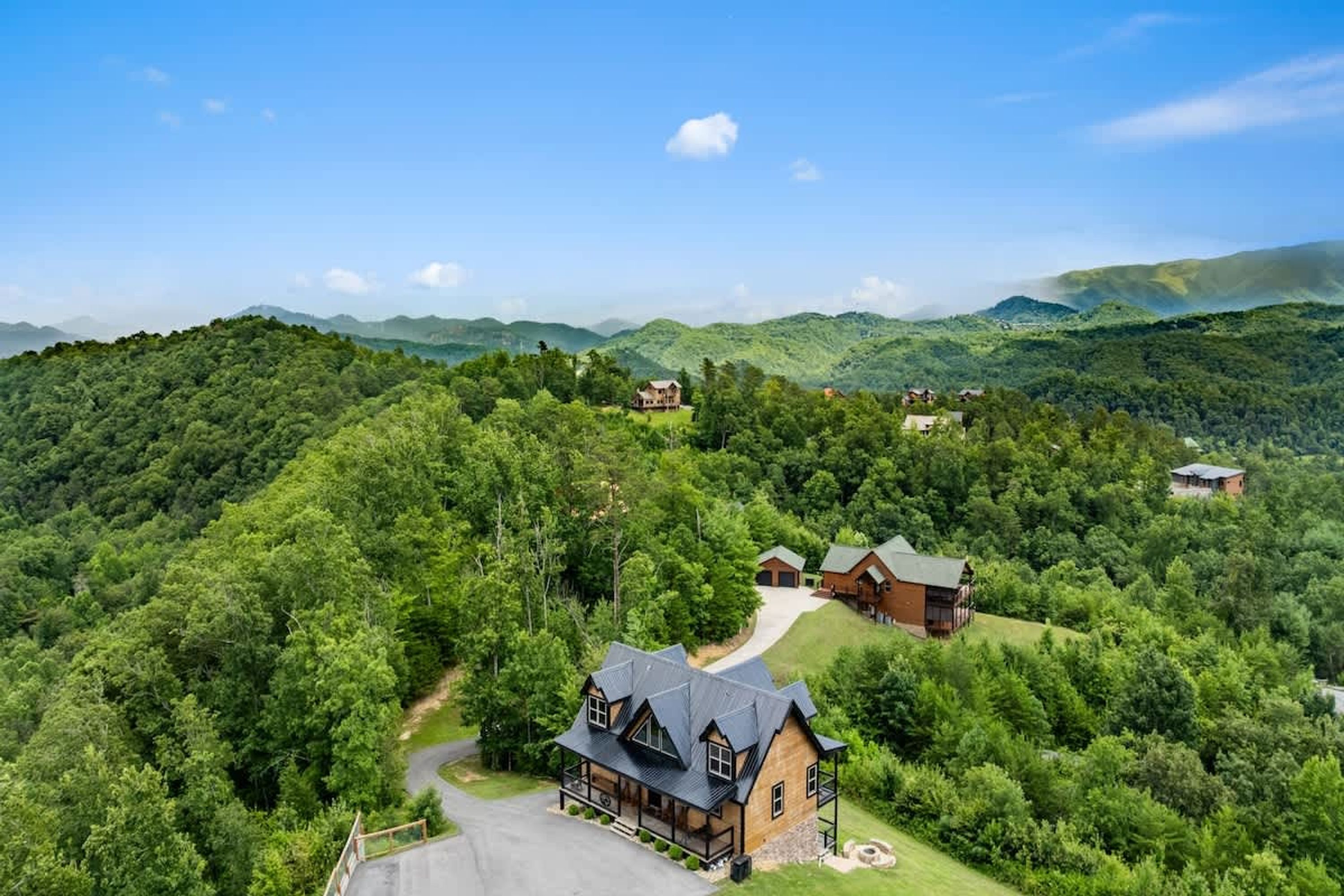 A large, rustic lodge with multiple buildings surrounded by dense forest and rolling hills.