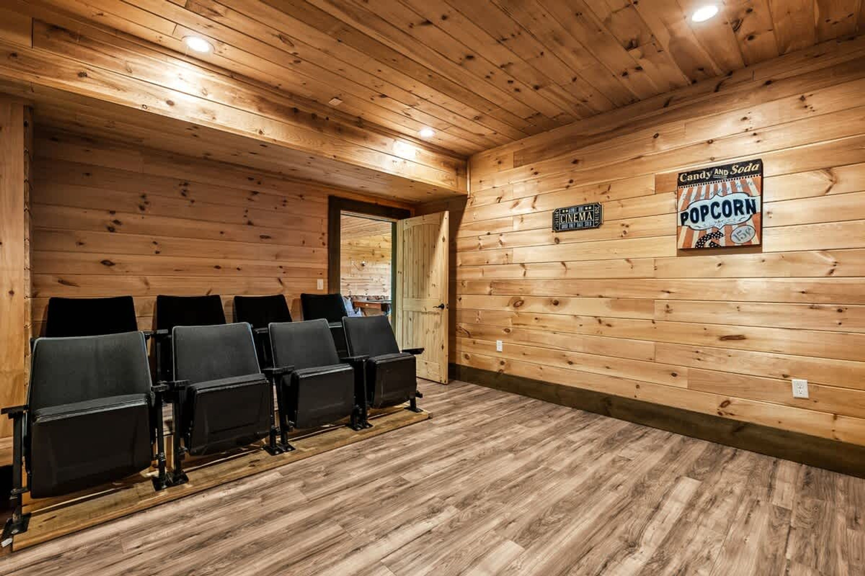 Una sala con rivestimenti in legno, sedie nere disposte a file, un cartello con scritto 'popcorn' e un cartellone cinematografico.