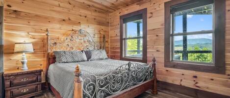 A wooden cabin bedroom with a bed, nightstand, lamp, and large windows.