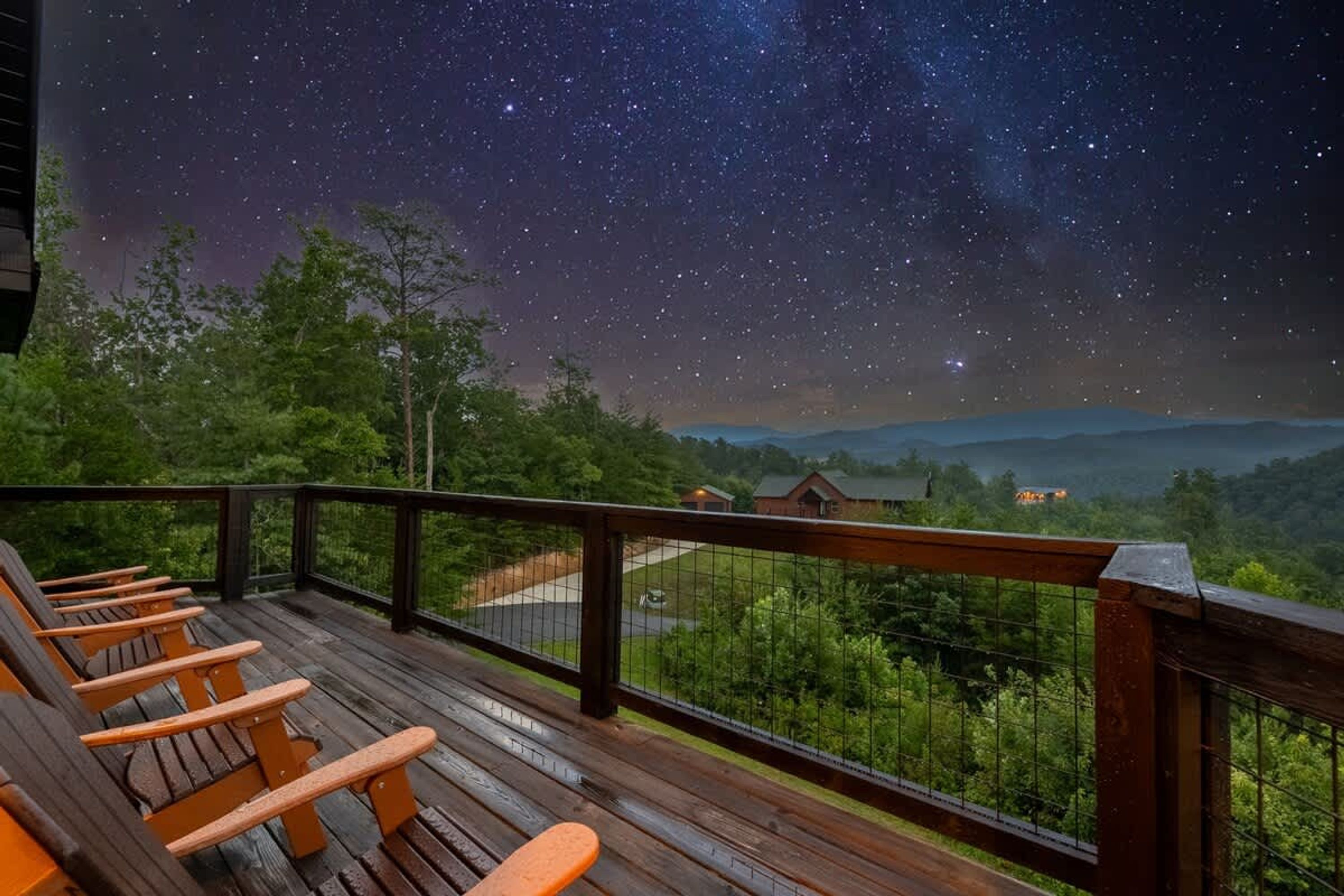 A wooden deck with orange chairs, a railing, and a night sky with stars.