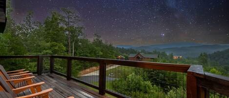 A wooden deck with orange chairs, a railing, and a night sky with stars.